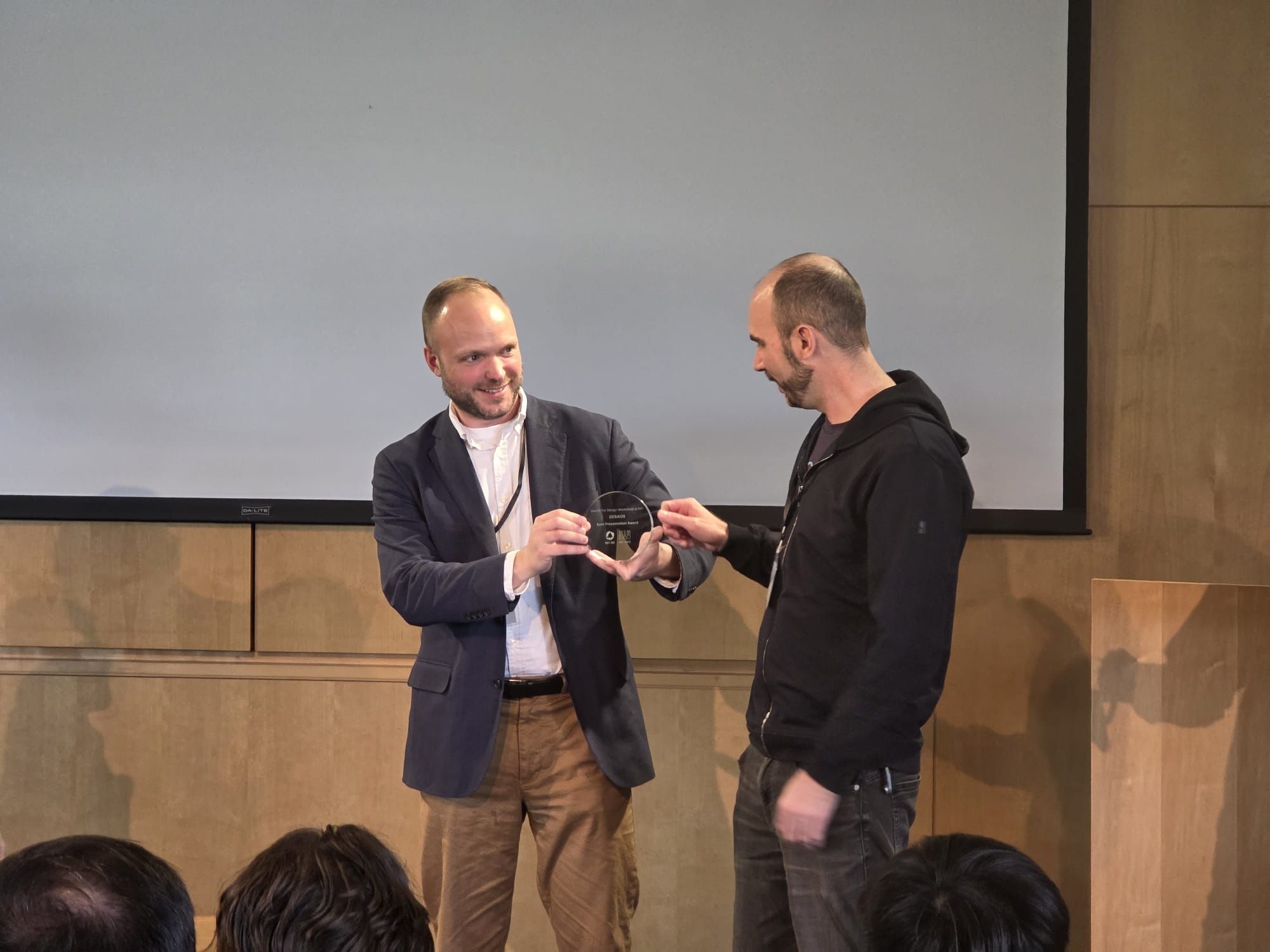 Martin and Daniel Pillis on a small stage holding a round engraved glass award between them